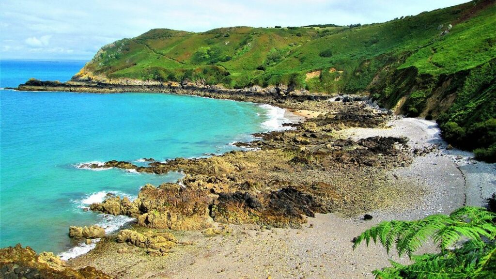 Crique de galets bordée de falaises verdoyantes et d'une eau turquoise, sur la côte nord de Jersey