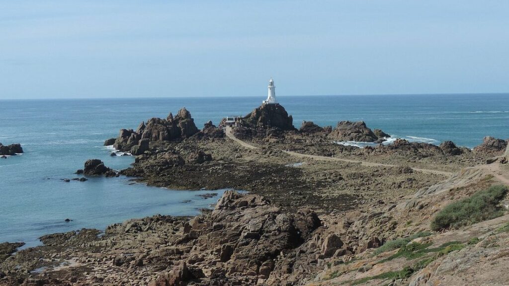 Phare blanc au bout d'un chaos de rochers qui s'avance dans la mer, sous un ciel dégagé