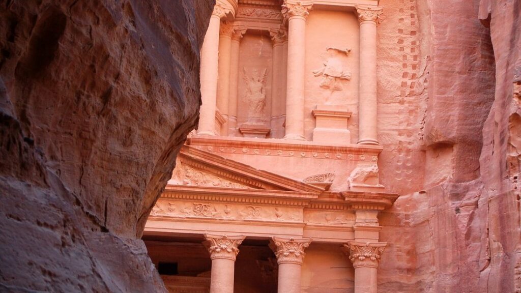 Façade rose du Trésor de Pétra apparaissant entre les parois sombres du Siq