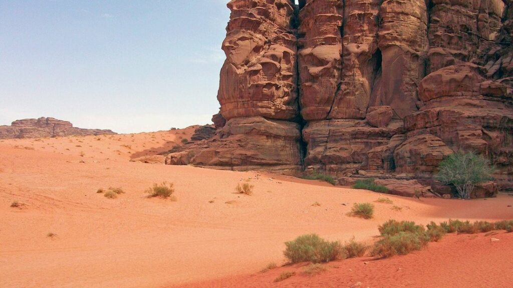 Sable orange et falaise de grès rouge dans le désert du Wadi Rum, sous un ciel clair