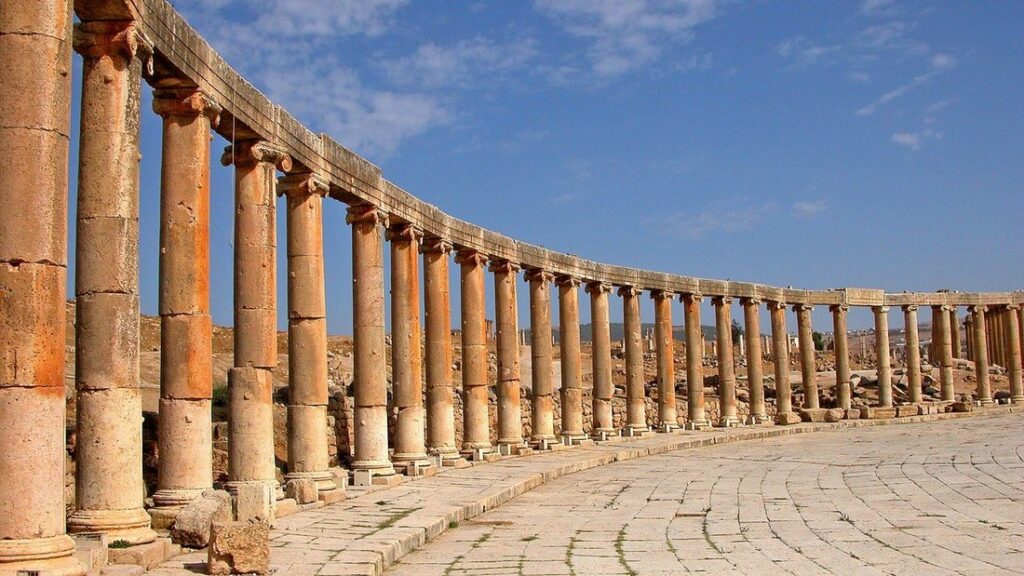Colonnade courbe de la place ovale de Jerash et pavés antiques sous un ciel bleu