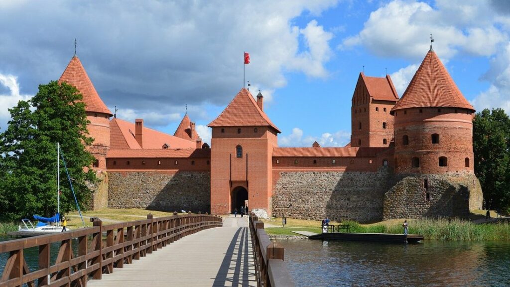 Château de briques rouges aux tours à toits pointus, atteint par une passerelle en bois sur le lac