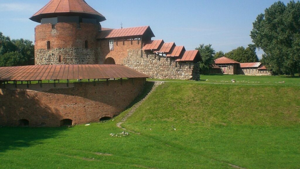 Tour ronde en briques rouges et remparts du château de Kaunas, au-dessus d'une pelouse verte