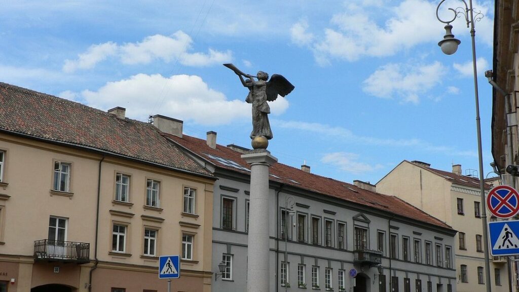 Statue d'un ange sur une colonne, au milieu d'une place bordée de façades anciennes