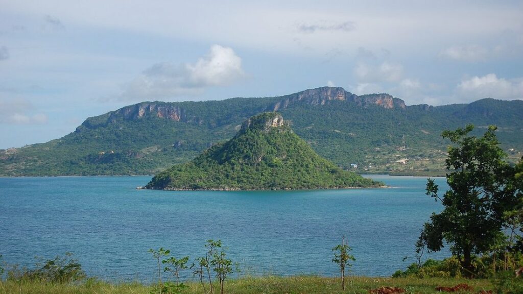Baie aux eaux bleues avec un îlot vert en forme de cône et des falaises boisées en arrière-plan