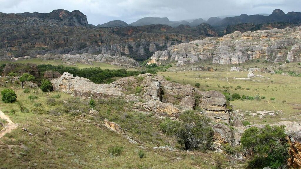Massif de grès aux parois découpées, au-dessus de collines d'herbe verte parsemées de rochers