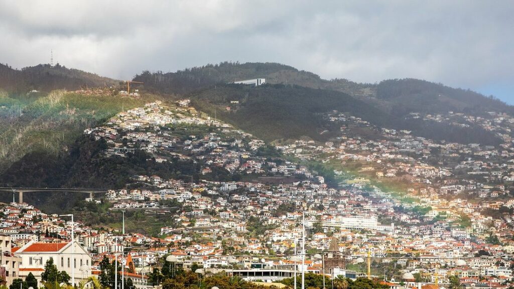 Maisons blanches aux toits orangés étagées sur les collines verdoyantes de Funchal, sous un ciel nuageux