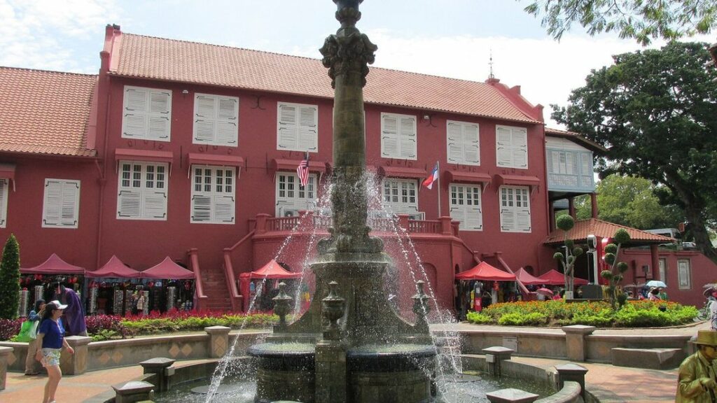 Bâtiment rouge du Stadthuys derrière une fontaine, sur la place des Hollandais, sous un ciel clair