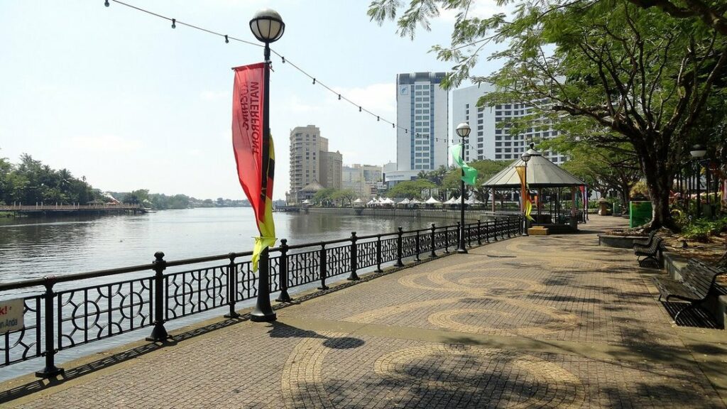 Promenade au bord de la rivière avec lampadaires et drapeaux, et des immeubles au fond