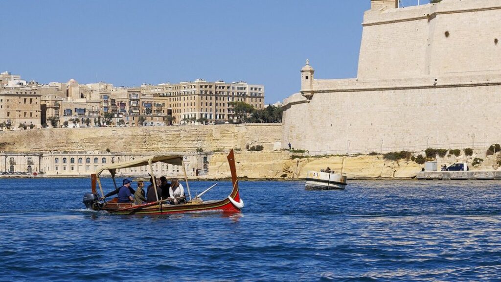 Barque traditionnelle colorée sur l'eau du port, devant les hautes murailles d'un fort et des maisons en pierre