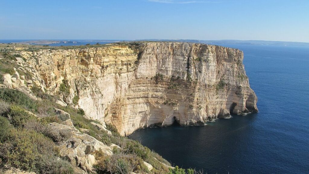 Haute falaise calcaire claire plongeant dans une mer bleue, sous un ciel dégagé