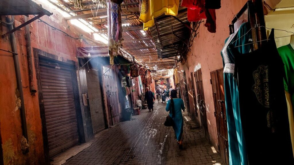 Ruelle étroite d'un souk aux murs ocre, avec des vêtements suspendus et des passants dans la lumière du matin