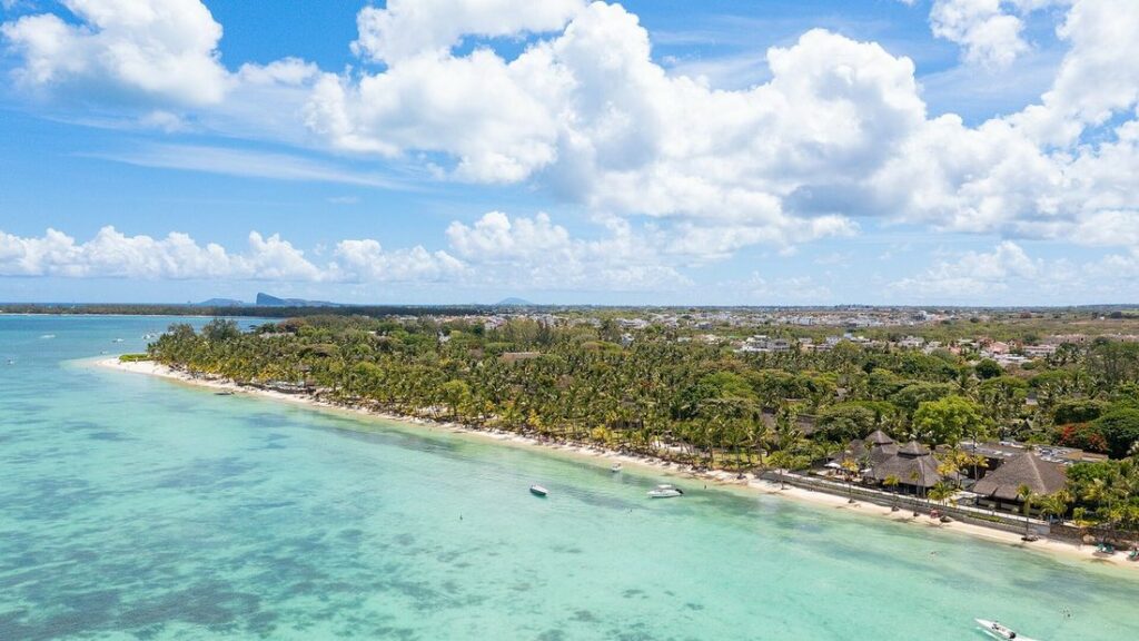 Vue aérienne d'une plage de sable clair bordée d'arbres, face à un lagon turquoise
