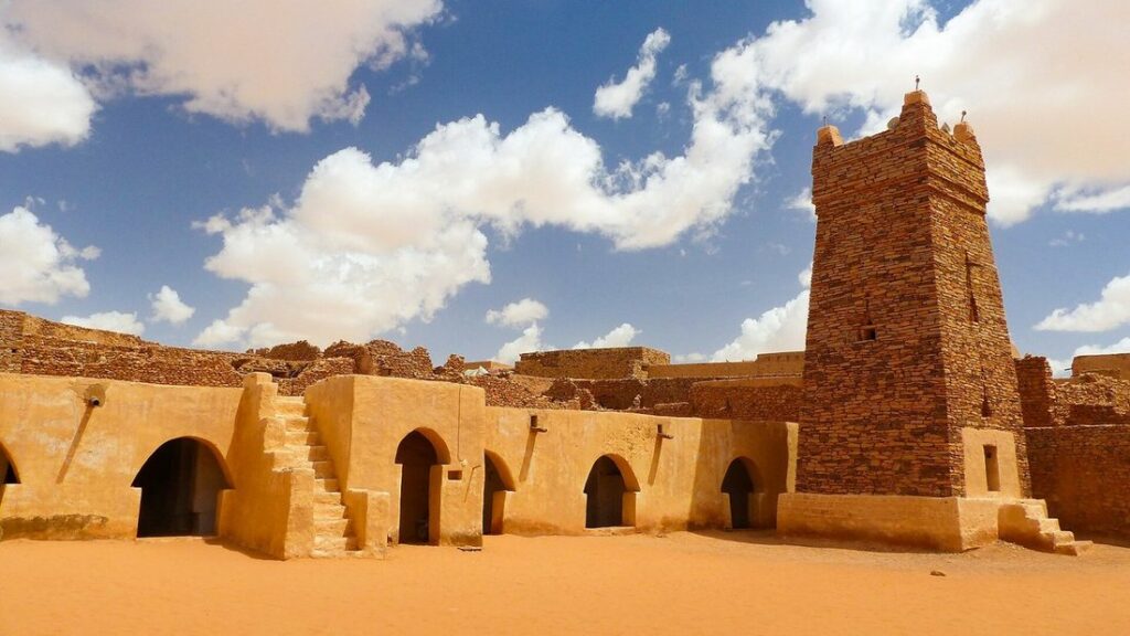 Mosquée en pierre ocre de Chinguetti avec son minaret carré et ses arcades, sous un ciel bleu et nuageux