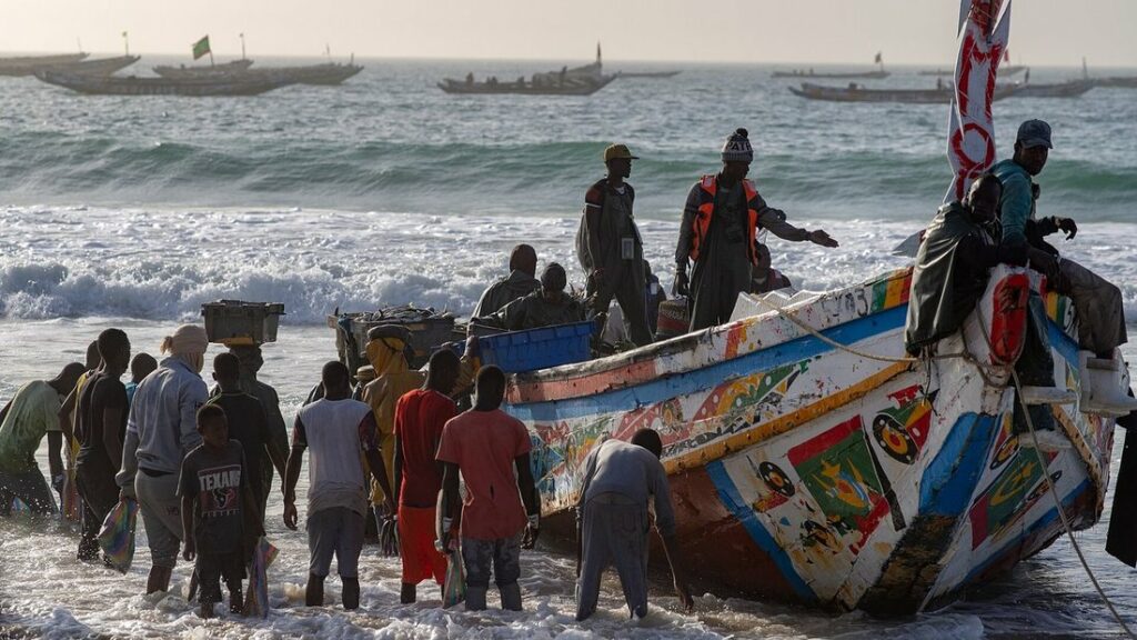 Pirogue en bois aux couleurs vives tirée sur la plage par des pêcheurs, avec des barques au large