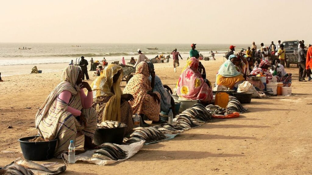 Marchands et clients assis sur le sable près de bâches étalées, au bord de la mer, au marché aux poissons