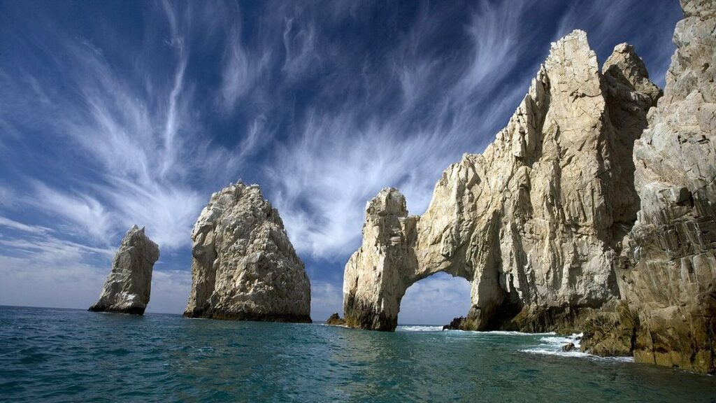 Rochers et arche d'El Arco émergeant de la mer, sous un ciel strié de nuages