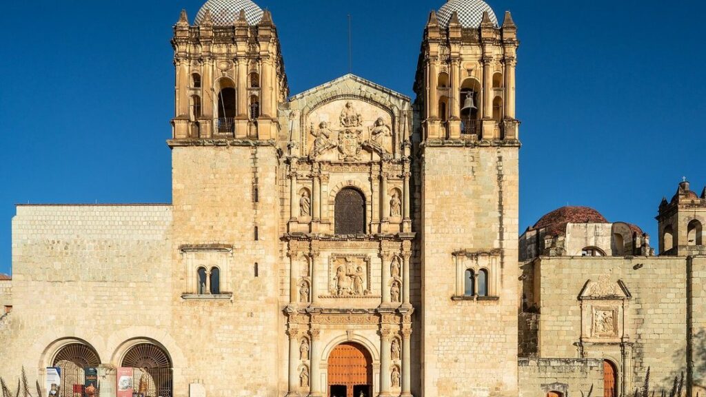Façade baroque en pierre dorée de l'église Santo Domingo de Guzmán à Oaxaca, sous un ciel bleu