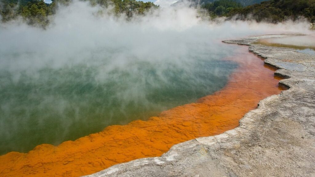Bassin géothermal aux eaux vertes et aux rebords orange, avec de la vapeur qui s'élève au-dessus de l'eau