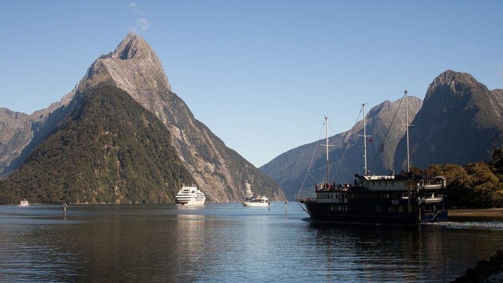 Le sommet pointu du Mitre Peak dominant l'eau calme du fjord, avec un bateau sur la droite