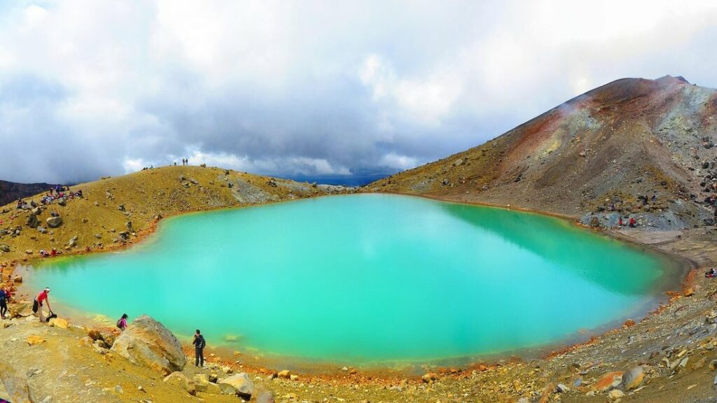 Lac d'un turquoise vif au milieu d'un terrain volcanique ocre, avec quelques randonneurs sur la rive
