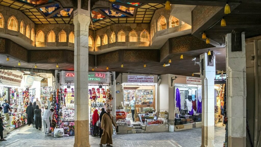 Allée couverte du souk de Mutrah, bordée de boutiques et de passants, sous un plafond ouvragé