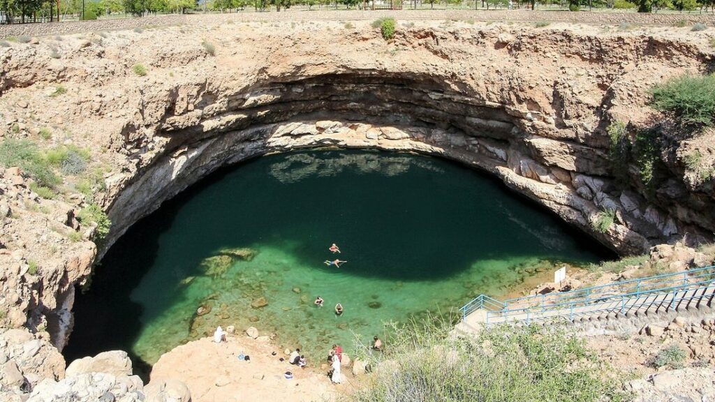 Large cuvette de calcaire emplie d'eau turquoise, avec quelques baigneurs, au Bimmah Sinkhole