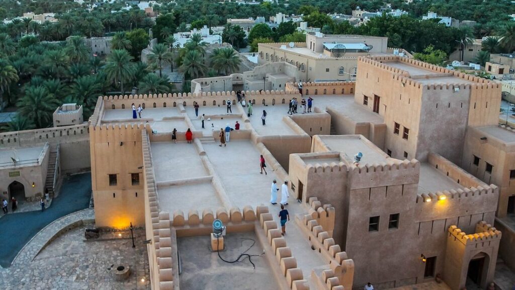 Vue plongeante sur les toits, les tours et les remparts du fort de Nizwa, avec la palmeraie au loin