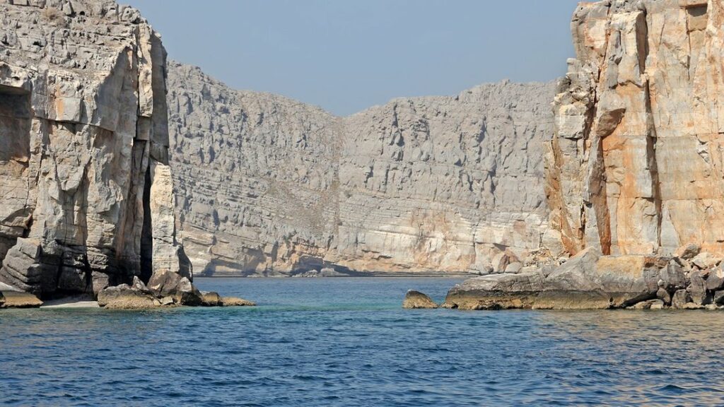 Hautes falaises de roche claire plongeant dans une eau bleue près de Khasab, dans le Musandam