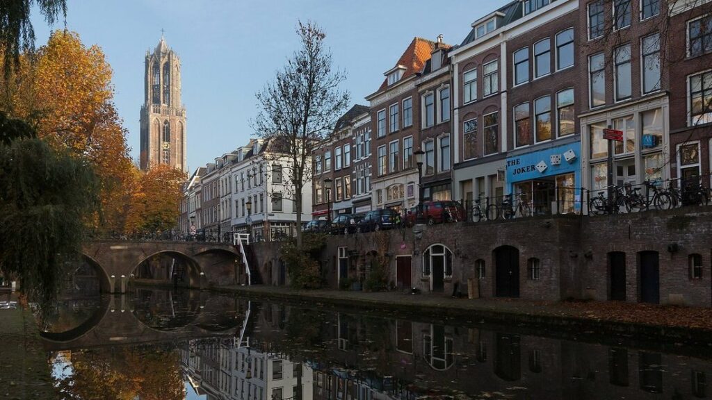 Canal bordé de façades de brique et de quais bas, avec la haute tour du Dom qui domine les toits