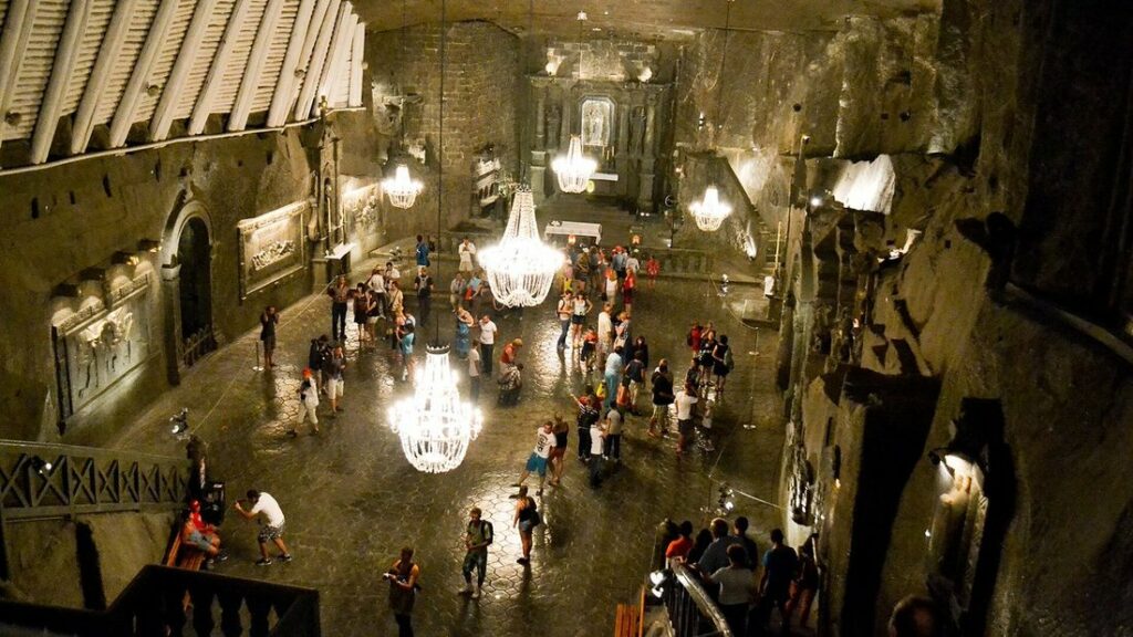 Vaste salle souterraine aux parois de sel éclairée par des lustres, avec des visiteurs réunis en groupe
