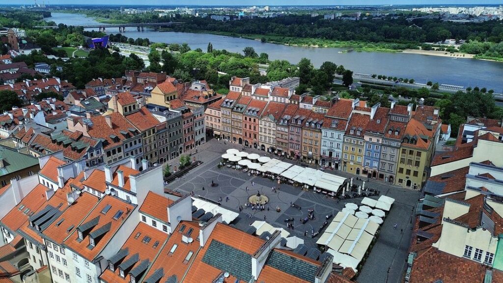 Vue aérienne d'une place entourée de maisons colorées aux toits rouges, avec la Vistule en arrière-plan