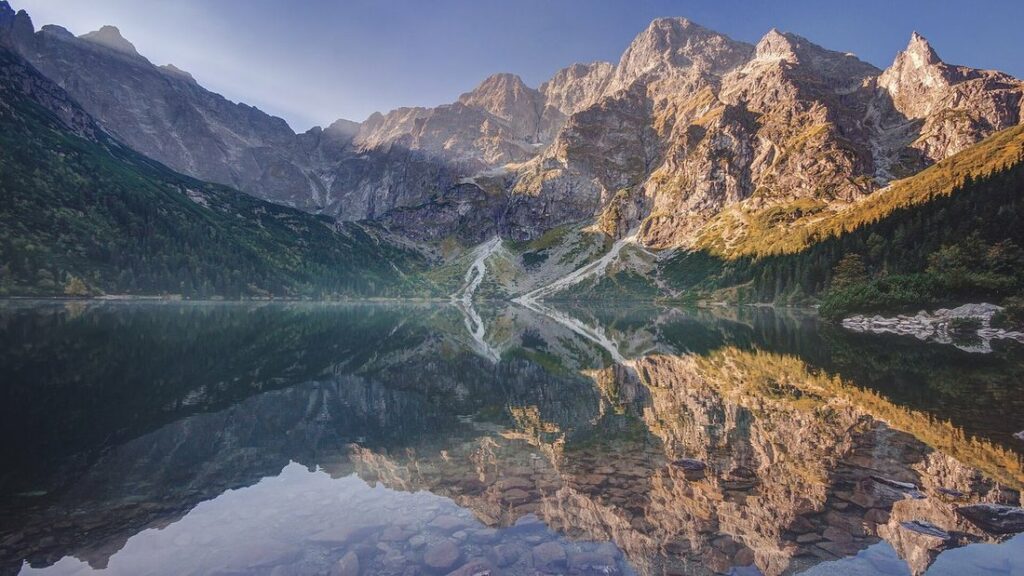 Sommets rocheux qui se reflètent dans l'eau immobile d'un lac de montagne, avec des forêts sur les pentes