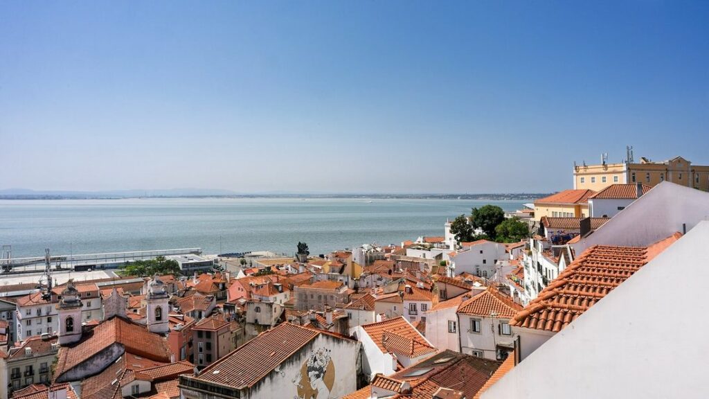 Toits de tuiles rouges d'Alfama et le Tage à l'horizon, vus depuis un belvédère de Lisbonne