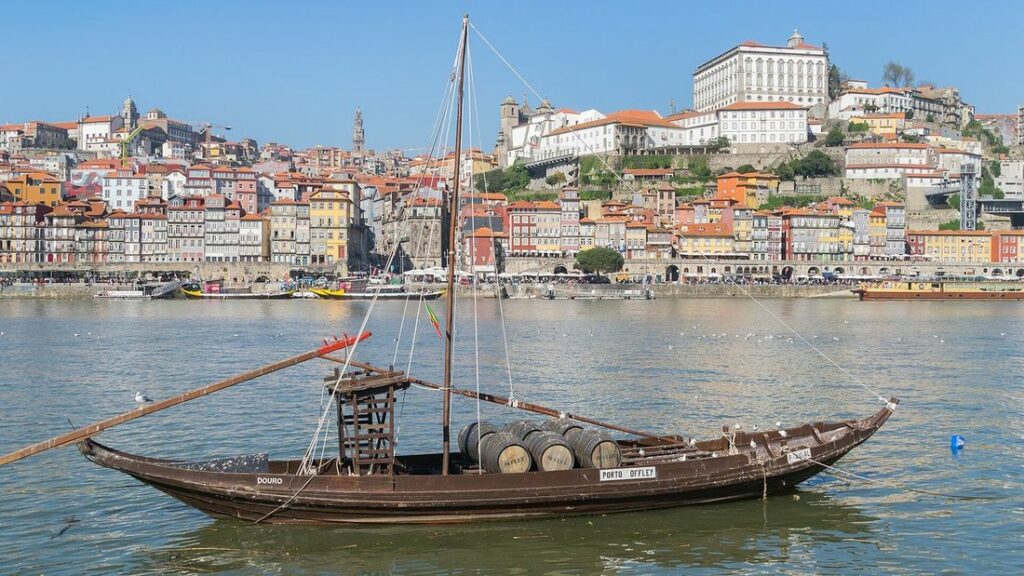 Un rabelo, bateau traditionnel chargé de tonneaux, sur le Douro devant les façades colorées de la Ribeira à Porto