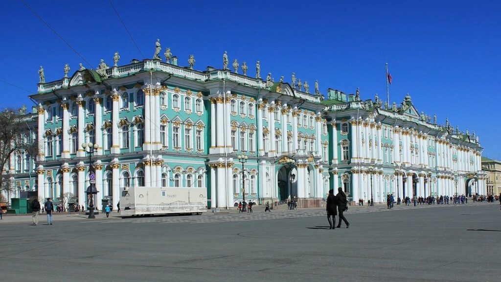 Façade verte et blanche du Palais d'Hiver, bordée par la place du Palais, avec quelques passants