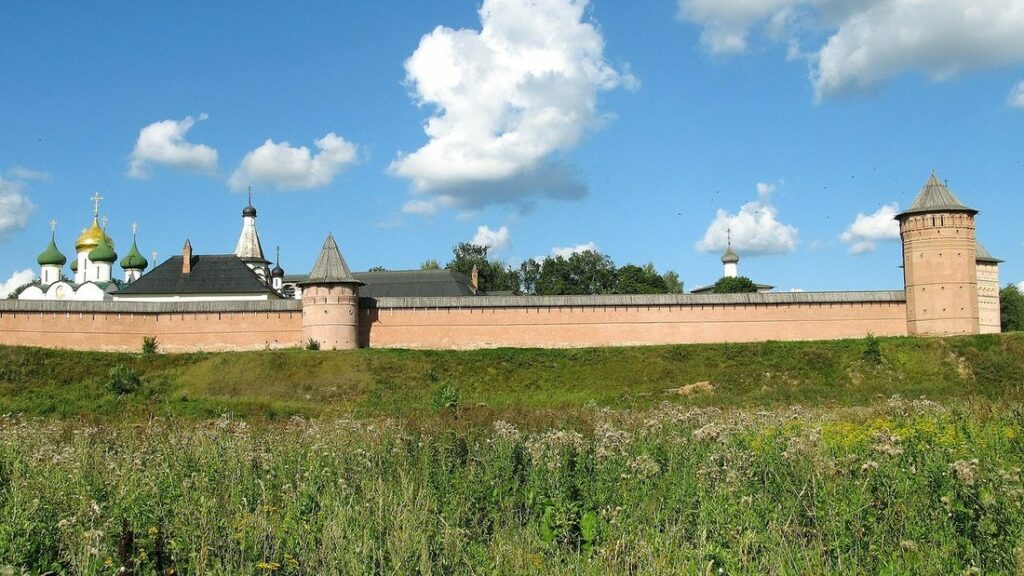 Mur de brique rouge à tours du monastère Saint-Euthyme de Souzdal, au-dessus d'une prairie sous un ciel bleu