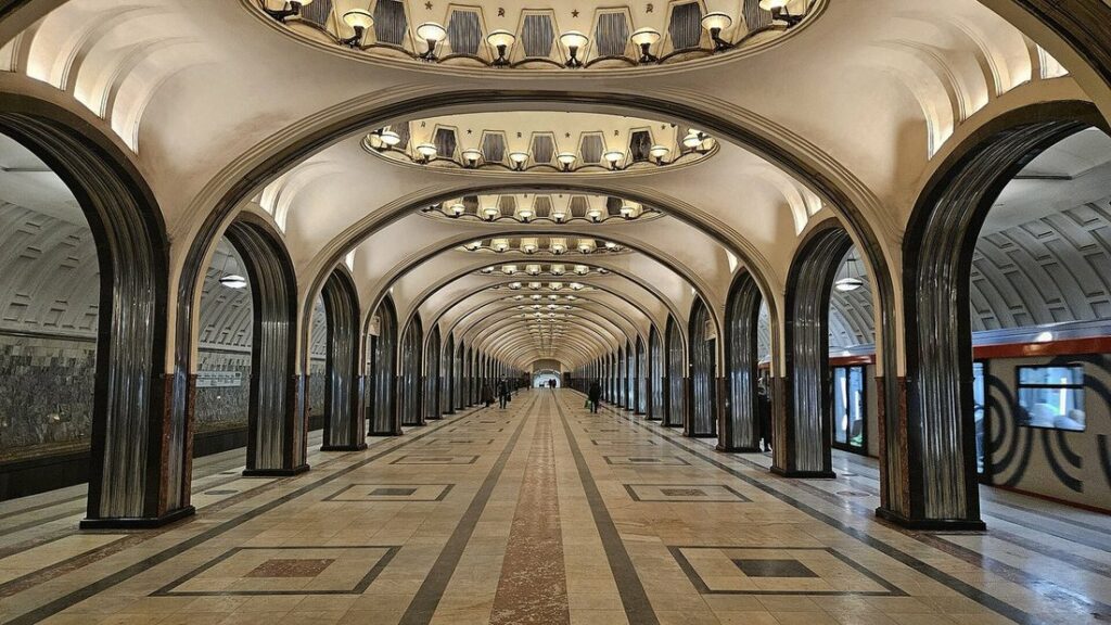 Station de métro à arches d'acier poli et plafond à médaillons lumineux, quai vide et rames de chaque côté