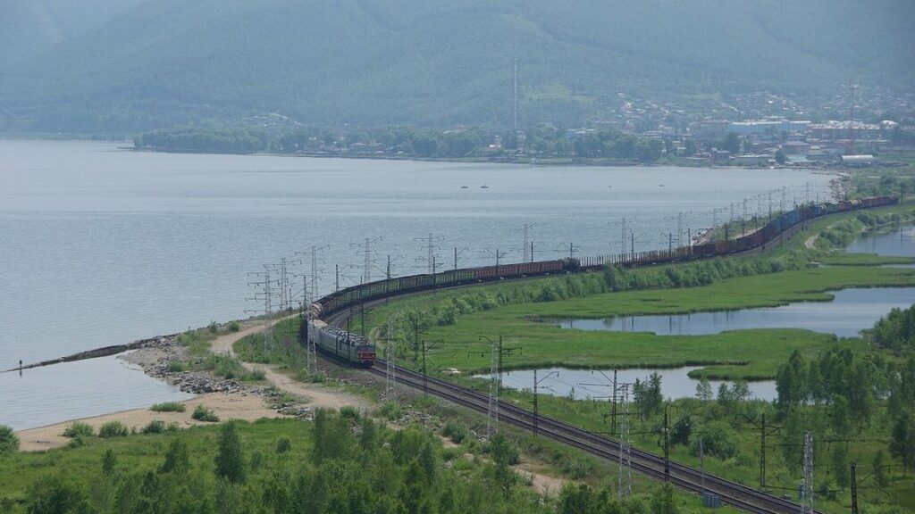 Long train sur une voie ferrée qui longe la rive du lac Baïkal, avec des montagnes dans la brume