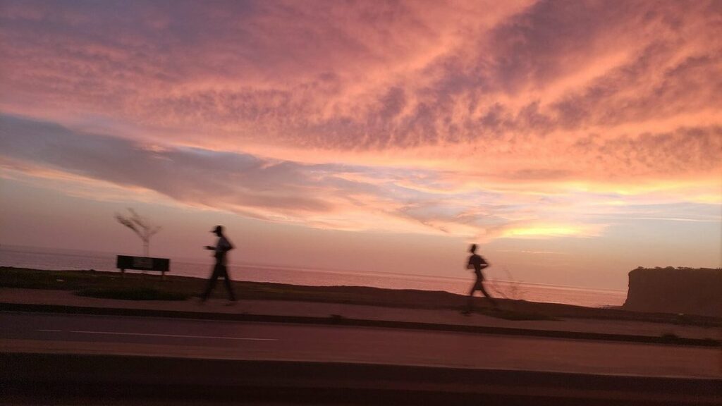 Deux joggeurs en silhouette sur la route de la corniche de Dakar, sous un ciel rose et orangé
