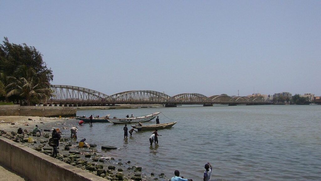 Le pont Faidherbe, pont métallique à arches, au-dessus du fleuve, avec des pêcheurs et des pirogues sur la rive