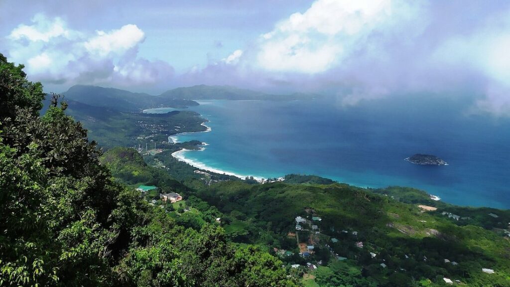 Vue depuis les hauteurs sur une baie turquoise bordée d'une plage, au pied de collines couvertes de forêt