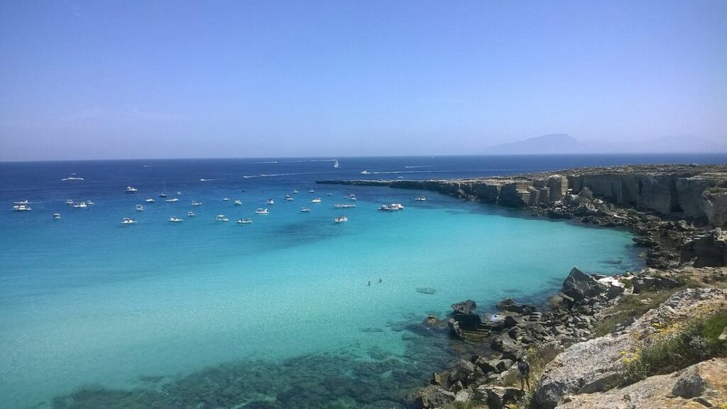 Crique turquoise de Cala Rossa, à Favignana, entourée de roche claire, avec quelques bateaux au mouillage