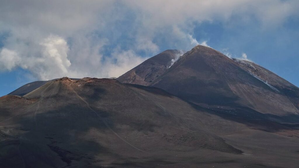 Les cratères sommitaux de l'Etna, aux pentes de lave sombre, sous un ciel bleu nuageux