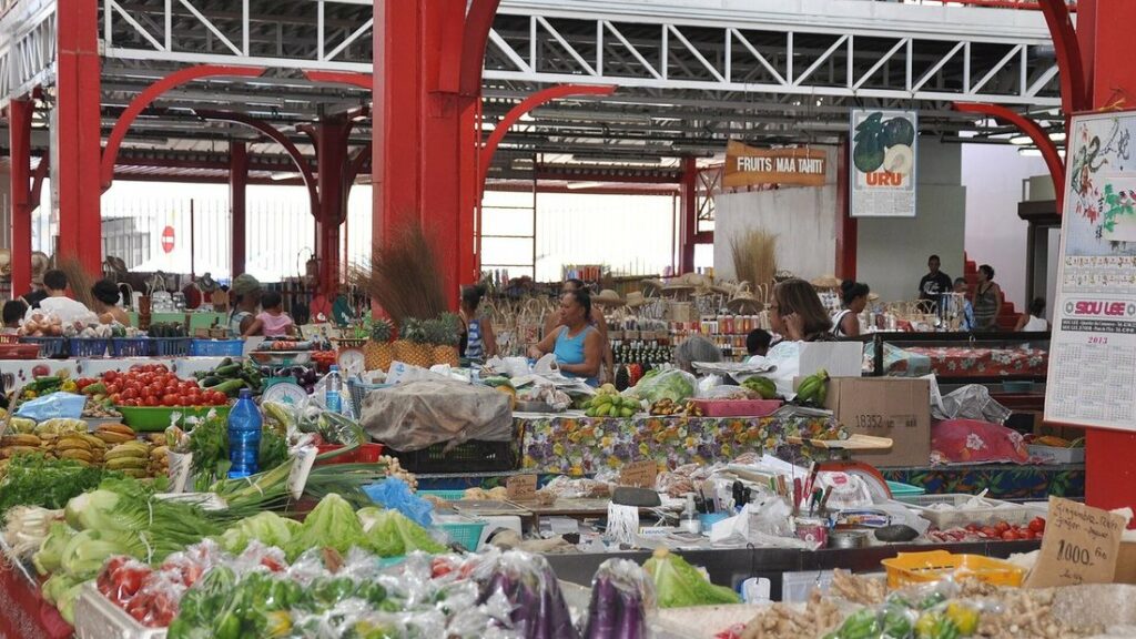 Étals de fruits et de légumes sous la grande halle à charpente rouge du marché de Papeete