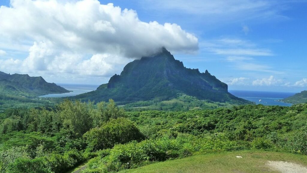Montagne verte coiffée de nuages entre deux baies bleues, vue depuis un belvédère, avec une forêt au premier plan
