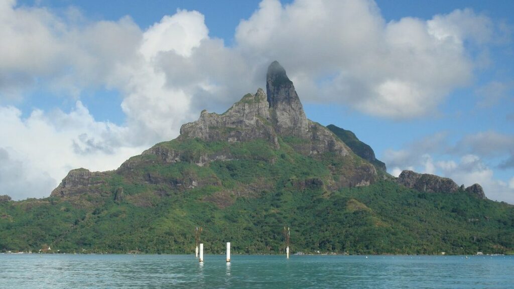 Pic rocheux couvert de végétation au-dessus d'un lagon calme, sous un ciel de gros nuages