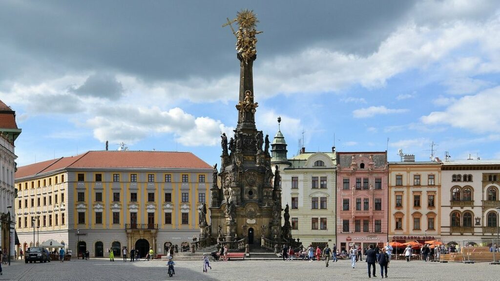 Colonne baroque de la Sainte-Trinité au centre de la grande place d'Olomouc, bordée de façades colorées