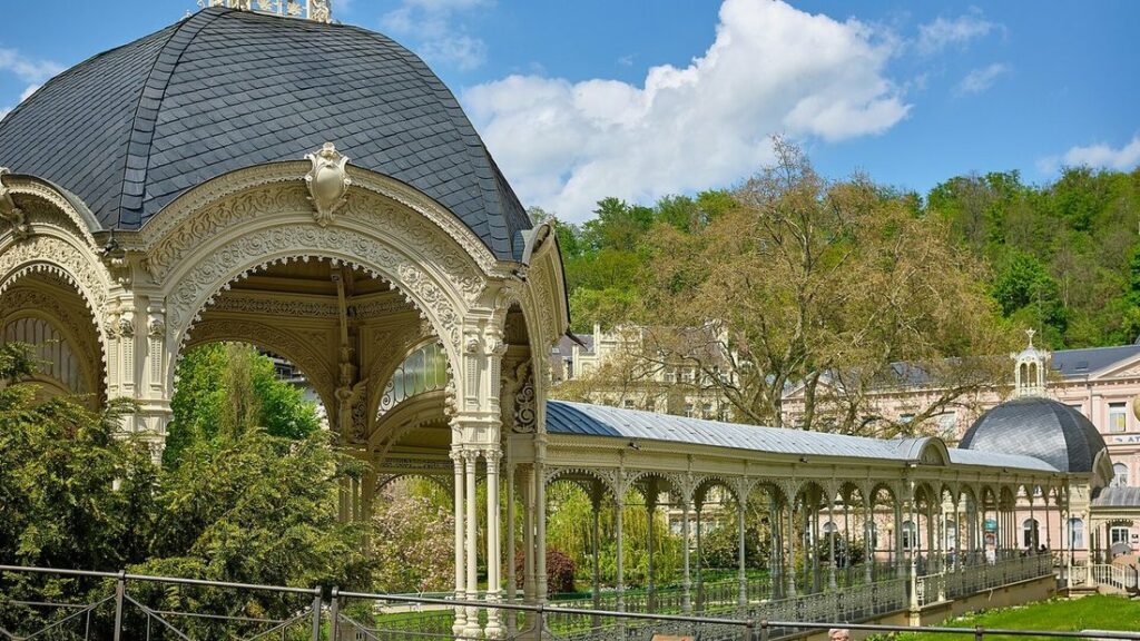 Pavillon à dôme d'ardoise et galerie blanche aux arcades ouvragées de la colonnade de Karlovy Vary, entre les arbres