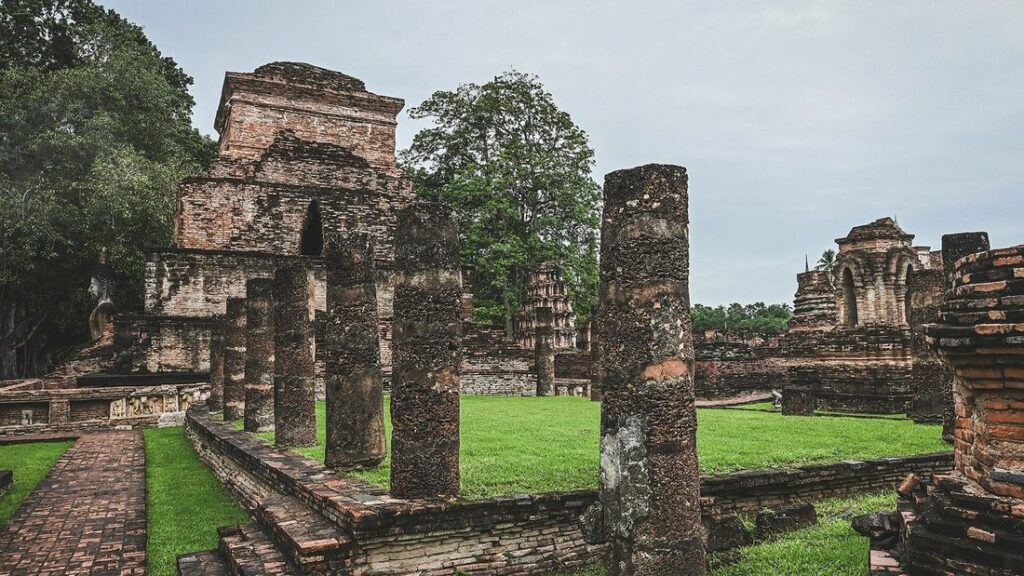 Colonnes et petits sanctuaires de brique en ruine posés sur une pelouse, dans le parc historique de Sukhothaï